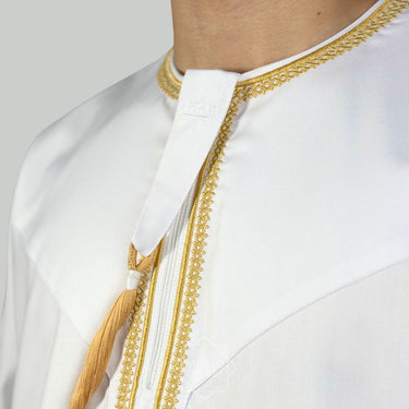 Model wearing a White collarless omani thobe with sophisticated gold embroidery on a plain background.